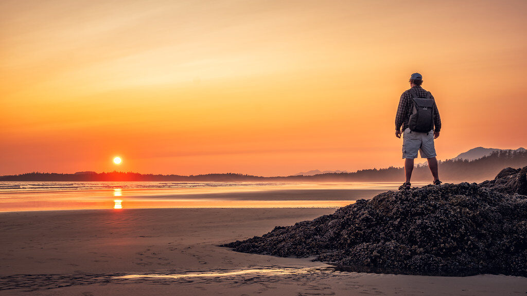 silhouette of man standing on rock near sea during sunset